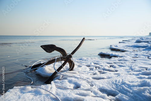 An patinous anchor alongside frozen seashore in winter