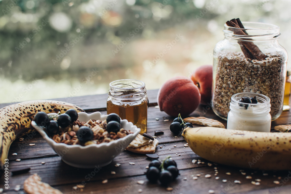 Healthy breakfast ingredients. Homemade granola, oatmeal, yogurt in the bottle, honey, berries and fruits on a wooden background. Morning aesthetics and beautiful layout on a wooden table.