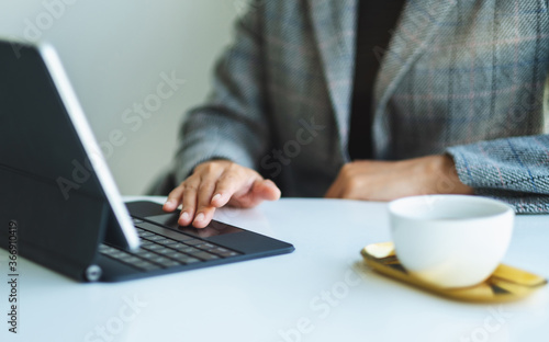 Closeup image of a woman working and typing on tablet keyboard as a computer pc with coffee cup on the table