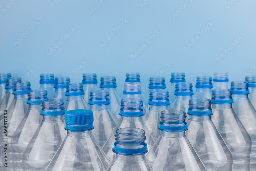 Empty clear plastic bottles with caps stacked on a blue background. Recycling and environment concept. Empty clear plastic bottles with caps stacked on a blue background. Recycling and environment concept.