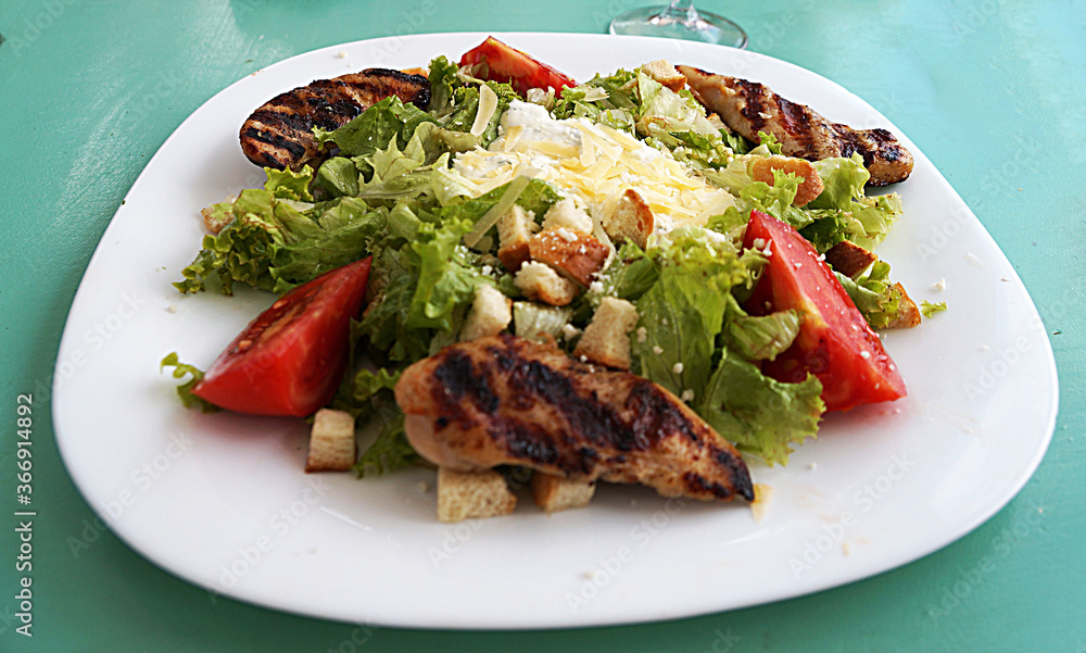 Caesar salad with chicken and cheese on a large white plate. Caesar salad with chicken and cheese on a large white plate.