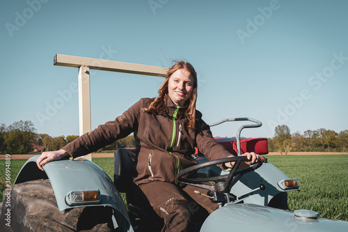 Junge Frau mit Spass an der Landwirtschaft sitzt auf einem Oldtimer - Traktor. photo