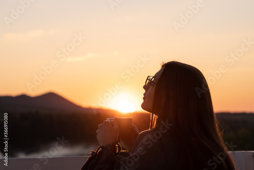 Girl with closed eyes drinking coffee contemplating views at sunset