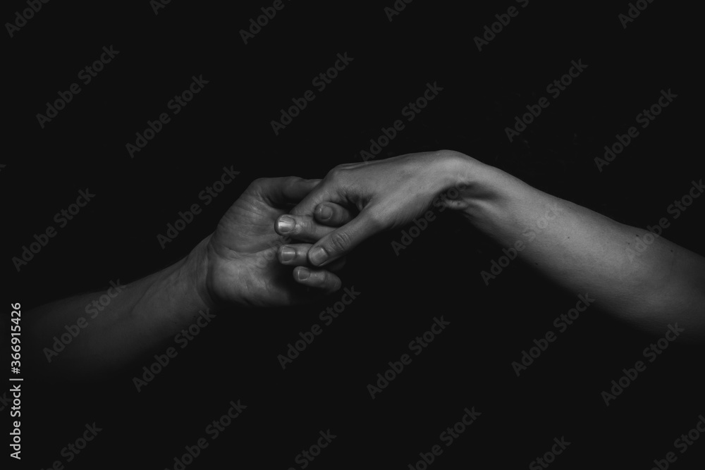touching fingers with hands and arms of a man and a woman in Black and white with a black background coming out of the dark
