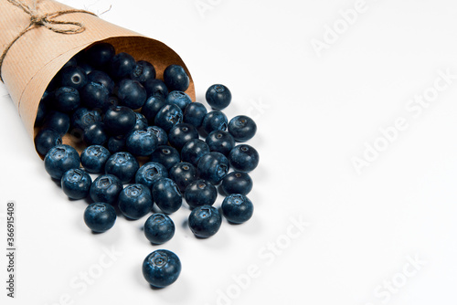 Freshly juicy picked blueberries in craft paper bag isolated on white background. Top view. Selective focus. Copy space. Concept of healthy eating and nutrition..