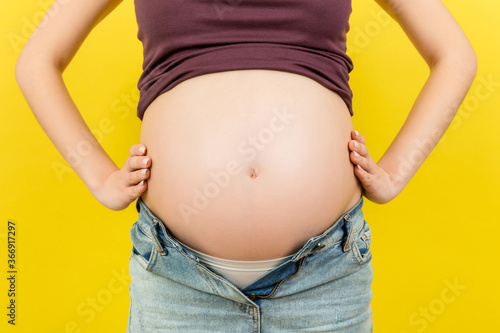 Close up of pregnant belly at colorful background with copy space. Future mother in opened jeans is embracing her naked baby bump. Motherhood concept © sosiukin