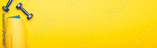 top view of rolled fitness mat and blue dumbbells on yellow background, panoramic shot