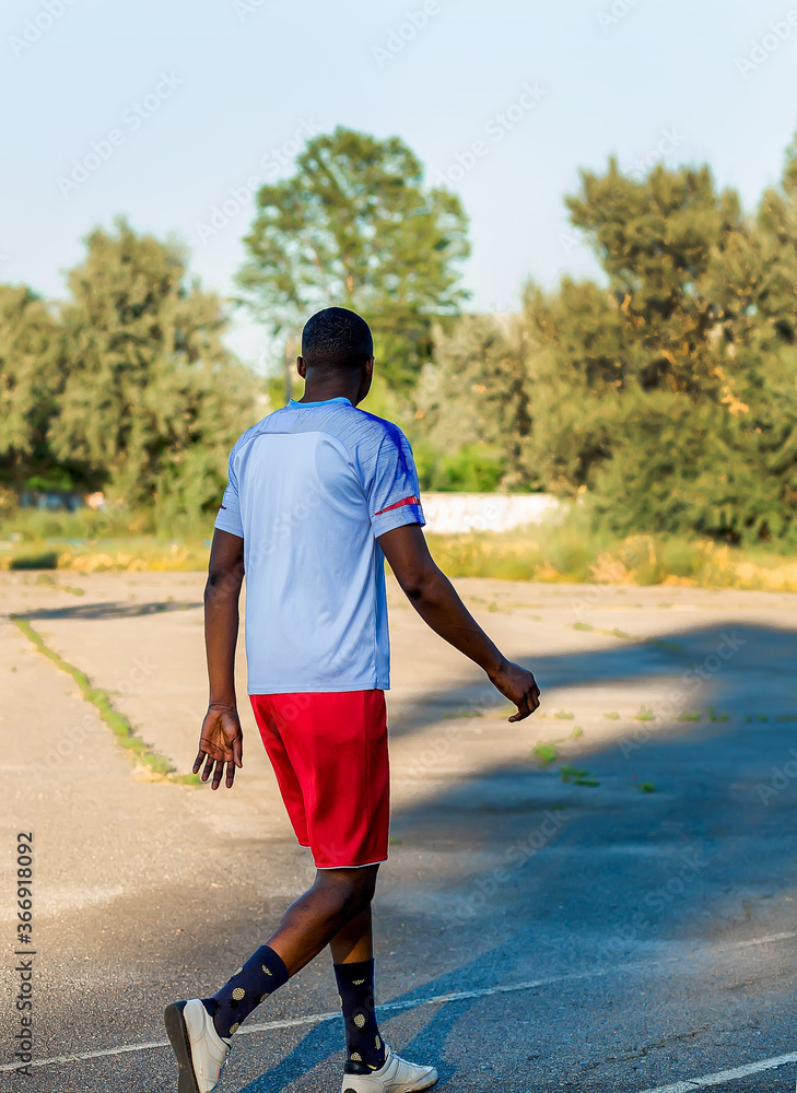 Young African American athlete in a white t-shirt and red shorts walking  calmly after jogging in a sports stadium. Man doing outdoor workout. Sport.  People active lifestyle concept Stock Photo | Adobe