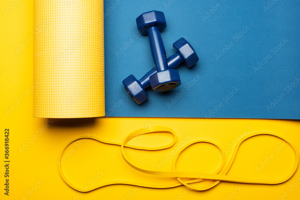 top view of blue fitness mat with dumbbells and resistance band on yellow background