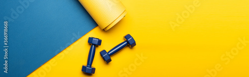 top view of blue fitness mat with dumbbells on yellow background, panoramic shot