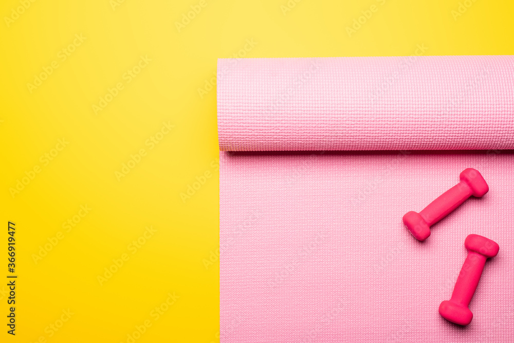 top view of pink fitness mat and dumbbells on yellow background top view of pink fitness mat and dumbbells on yellow background