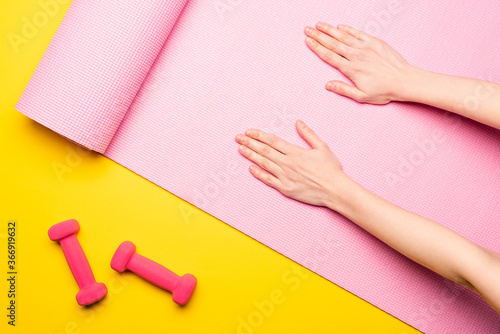 top view of female hands on pink fitness mat near dumbbells on yellow background