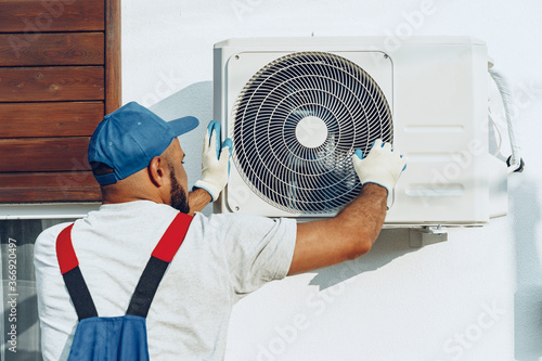 Quadro su tela Repairman in uniform installing the outside unit of air conditioner