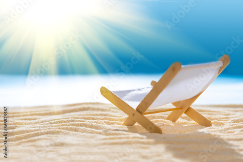 Deck chair on sandy beach with blurry blue ocean and sun beams on sky. Social distancing or COVID-19 protection at summer holidays. Summer background. Soft focus