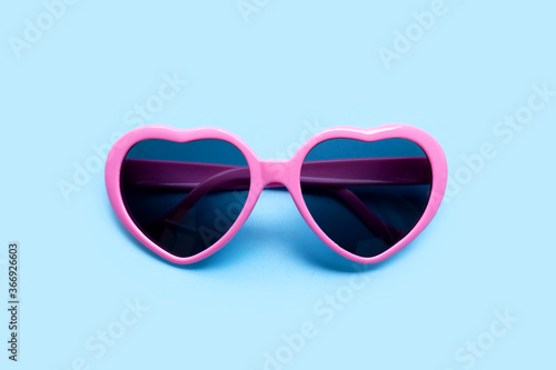 Pink heart shaped sunglasses on blue background.
