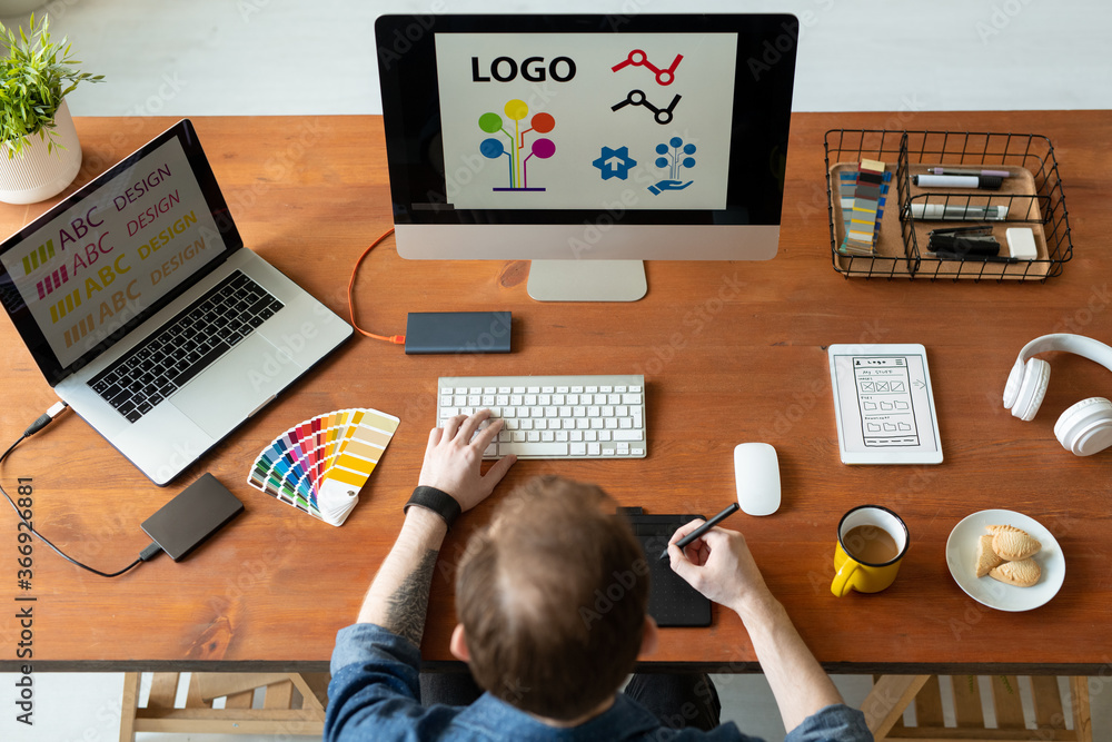 Above view of logo designer sitting at desk and editing icon design using drawing pad Above view of logo designer sitting at desk and editing icon design using drawing pad