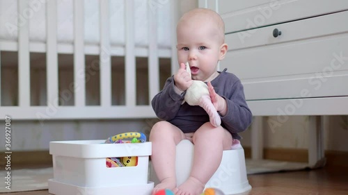 Little toddler girl, sitting on potty, playing with plastic toy at home
