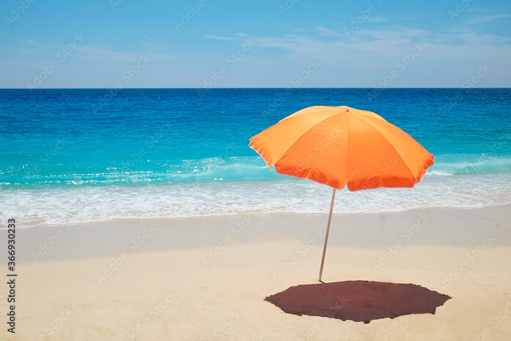 Single orange umbrella on a perfect beach with clean golden sand and clear turquoise water on a windless and sunny summer day. Tropical background, copy space, top view.