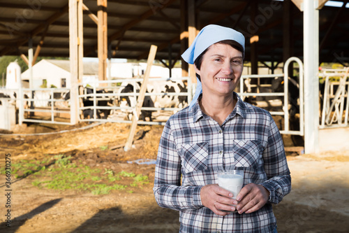 Active woman is holding glass of milk at the cow farm