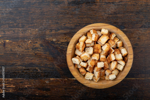 Crispy croutons in a bowl on a wooden background.