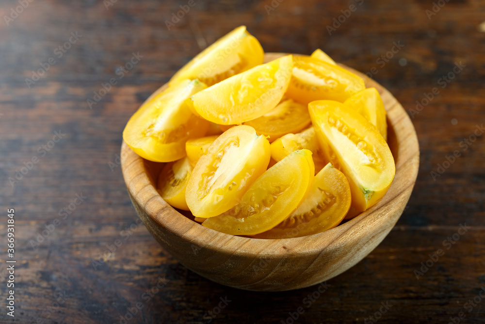 Sliced yellow tomato in a bowl on a wooden background. Vegetable, ingredient and staple food. Sliced yellow tomato in a bowl on a wooden background. Vegetable, ingredient and staple food.