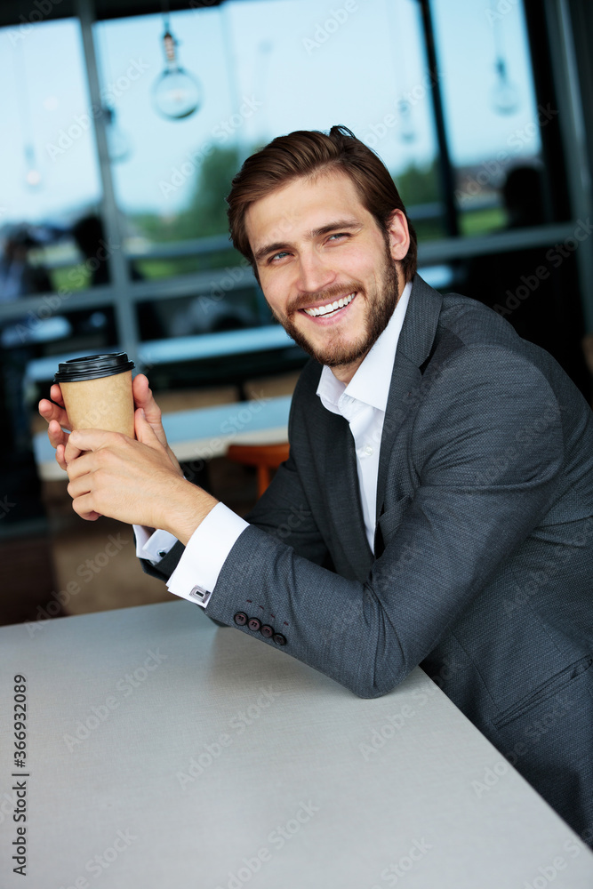 Charming young bearded businessman smiling, holding a paper cup of coffee Charming young bearded businessman smiling, holding a paper cup of coffee