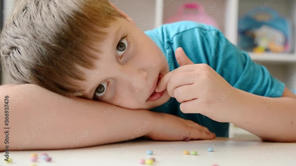 Cheerful boy plays and eats chocolate multi-colored round candies. Cheerful boy plays and eats chocolate multi-colored round candies.