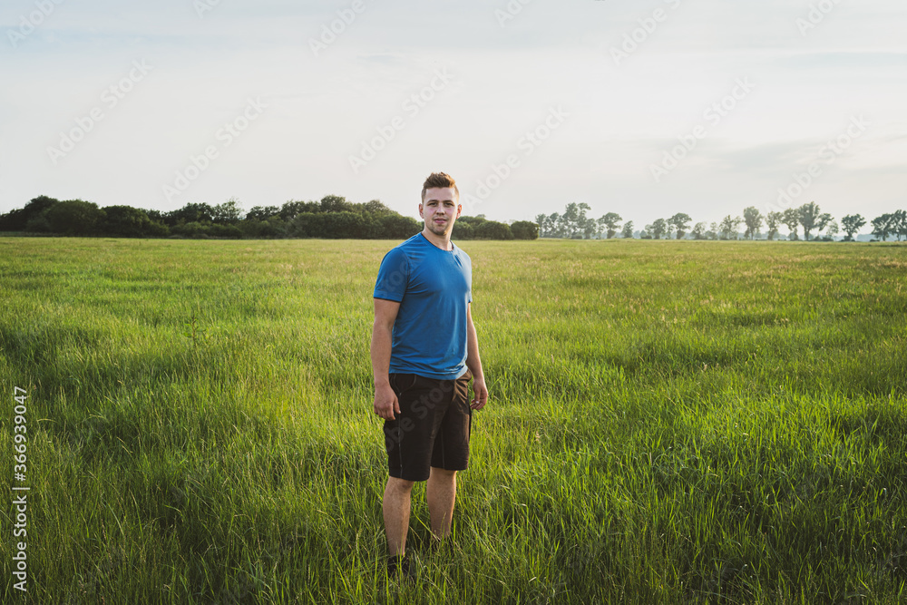 Landwirtschaft - Feldfutterbau, junger Landwirt steht auf einer großen Grünlandfläche.