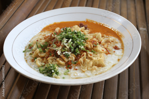 Bubur ayam or chicken porridge, Indonesian rice porridge with shredded chicken and chunks of cakwe. Breakfast dish of rice porridge with chicken, Chinese croissant, celery, and fried shallot