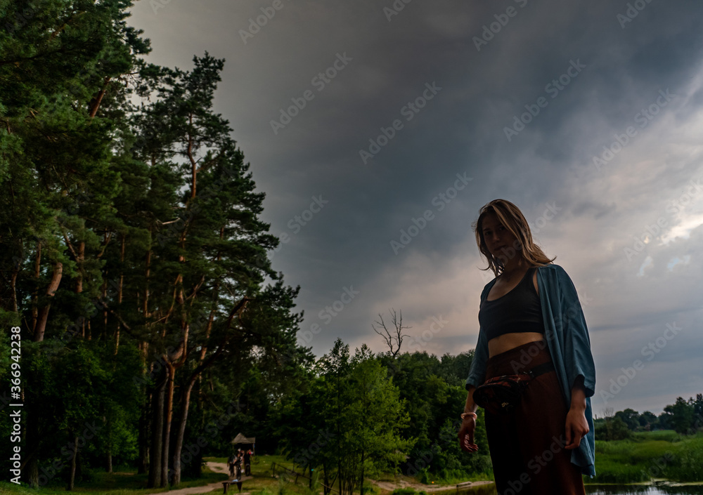 Young woman in full growth on background of pine trees and an approaching thunderstorm