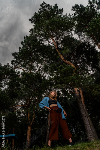 Young woman in full growth on background of pine trees and an approaching thunderstorm