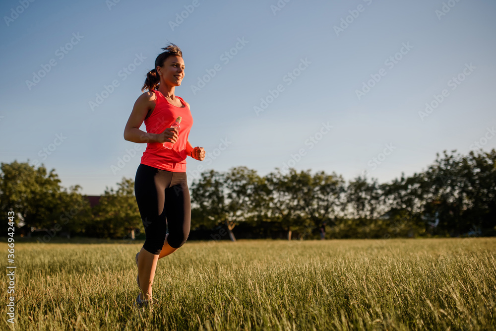 Young beautiful woman is making sport, she is running on a grass in the midst of nature on sunset. Young beautiful woman is making sport, she is running on a grass in the midst of nature on sunset.
