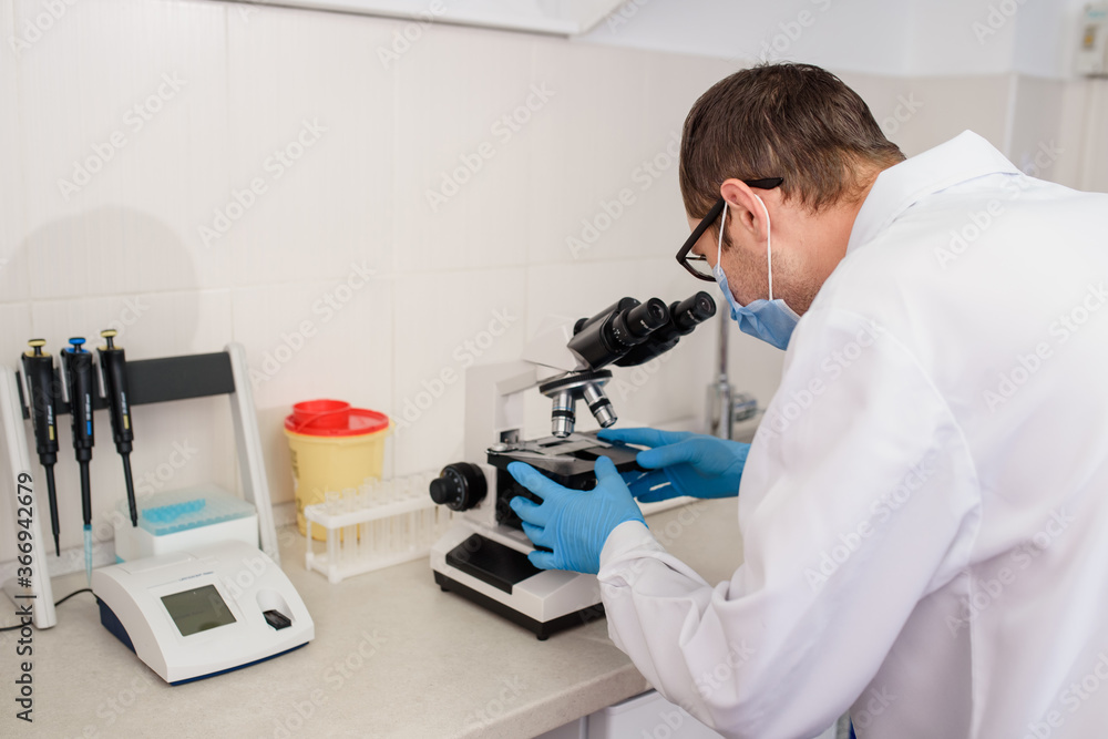 In the hospital laboratories working process, a young man doctor is looking in the medical microscope In the hospital laboratories working process, a young man doctor is looking in the medical microscope