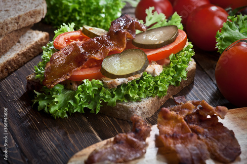 closeup of smoked meat sandwich with green salad, fresh tomatoes, pickled cucumbers and bread, on dark wooden table background