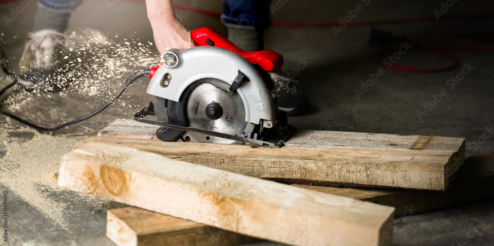 Man with circular saw for cutting boards. Construction and home renovation in the workshop. Worker saws a wooden plank at a construction sit. Man with circular saw for cutting boards. Construction and home renovation in the workshop. Worker saws a wooden plank at a construction sit.