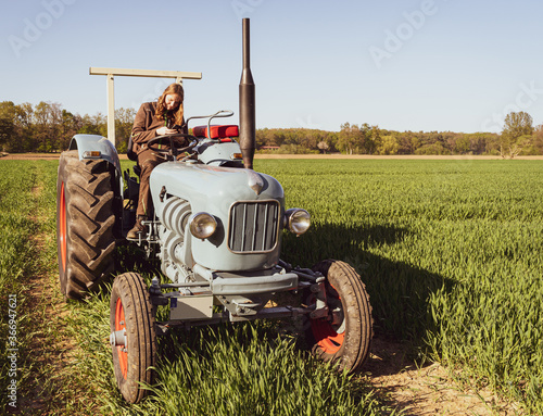 Junge Frau mit Spass an der Landwirtschaft sitzt auf einem Oldtimer - Traktor. photo