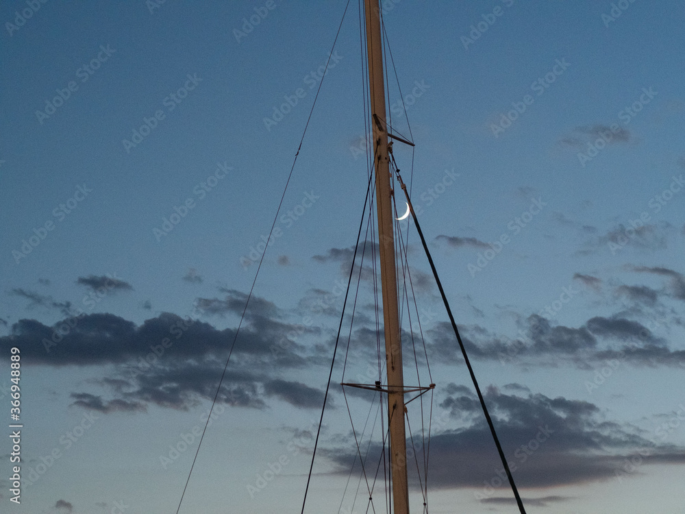 the moon is between the mast a blue sky