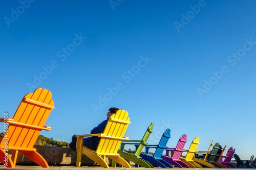 Man relaxing in a row of brightly colored adirondack chairs along waterfront in fall/autumn photo