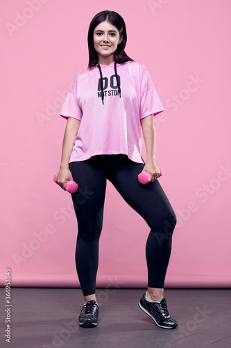 ?orgeous body positive Latin woman in a pink hoodie with dumbbells photo