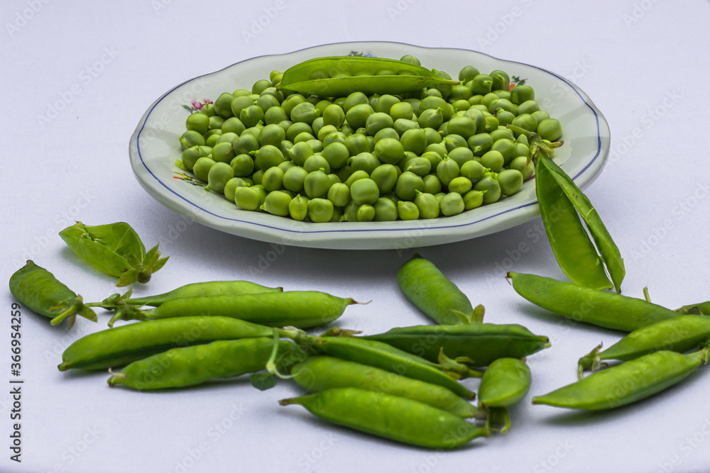 Green Peas. Green background. Peas background. Top view.Green pea in bowl on white background copy space. Fresh organic green peas on a round white plate. Vegetable harvesting Green Peas. Green background. Peas background. Top view.Green pea in bowl on white background copy space. Fresh organic green peas on a round white plate. Vegetable harvesting