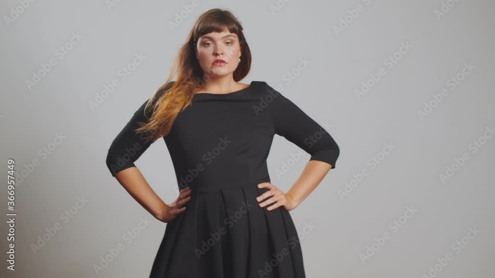 Plus size elegant model with stylish hairstyle in black dress posing at grey background in studio isolated Plus size elegant model with stylish hairstyle in black dress posing at grey background in studio isolated
