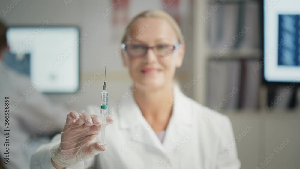 Portrait female senior doctor in protective gloves holding syringe with vaccine on office background Portrait female senior doctor in protective gloves holding syringe with vaccine on office background