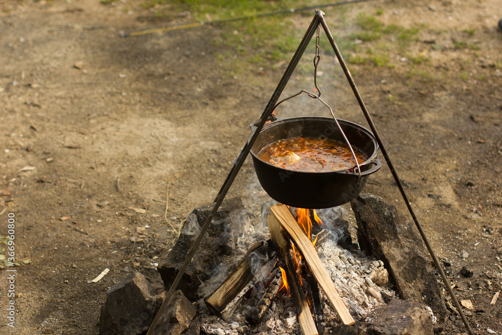 Cooking camping outdoor meal in an open fire in a travel pot with blaze. Dinner during travel. Cooking camping outdoor meal in an open fire in a travel pot with blaze. Dinner during travel.