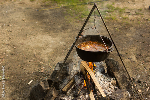 Cooking camping outdoor meal in an open fire in a travel pot with blaze. Dinner during travel.