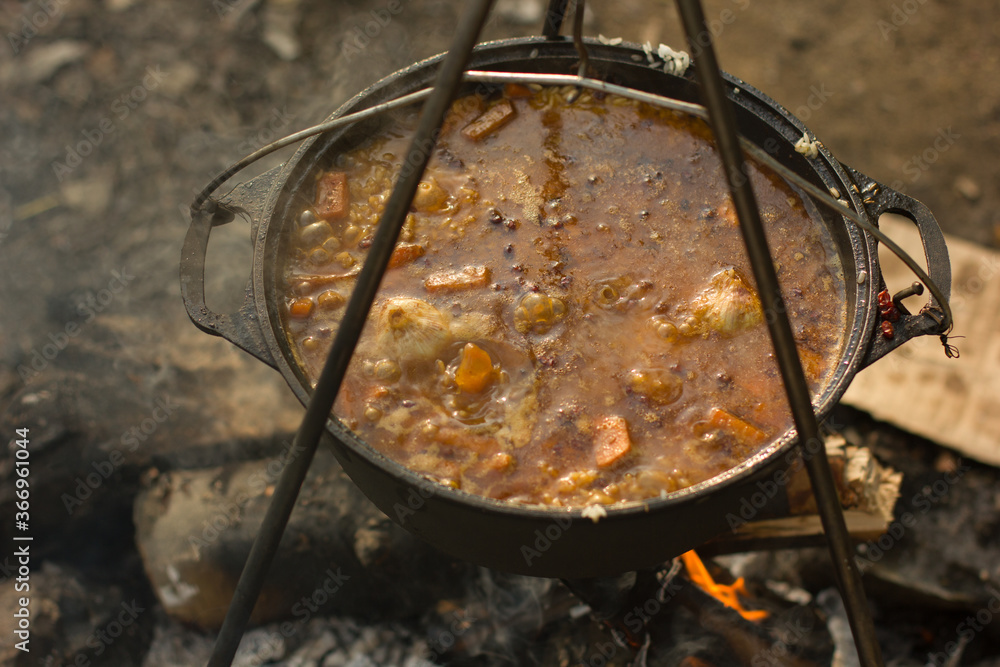 Cooking camping outdoor meal in an open fire in a travel pot with blaze. Dinner during travel. Cooking camping outdoor meal in an open fire in a travel pot with blaze. Dinner during travel.