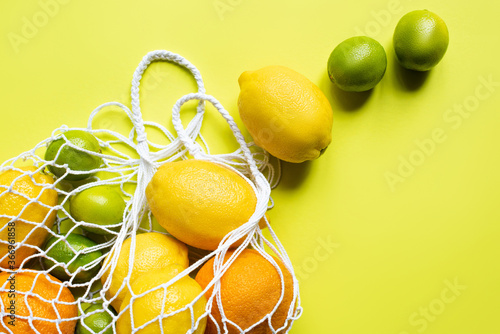 Fototapeta Naklejka Na Ścianę i Meble -  ripe whole citrus fruits in string bag on yellow background
