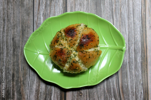 Korean Garlic Cheese Bread or Yugjjog Maneulppang is made from bread, cream cheese, garlic, parsley, and honey served on a leaf-shaped green plate on a wooden table. photo