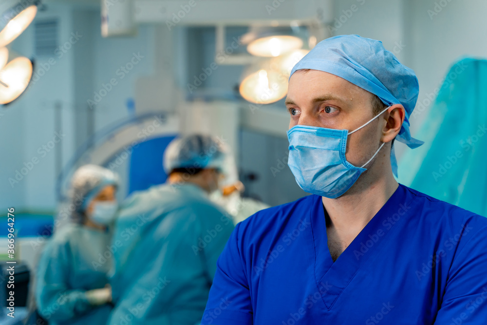 Selective focus on medic in operating room. Mask on face. Blurred background with working team. Selective focus on medic in operating room. Mask on face. Blurred background with working team.