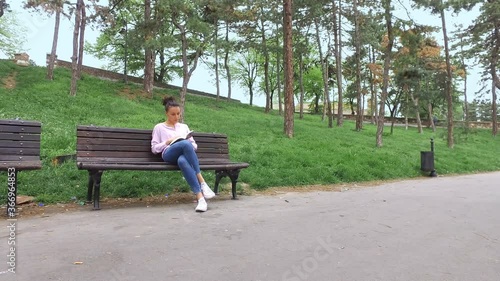 Beautiful girl sitting on a wooden bench and reading a book in the green park