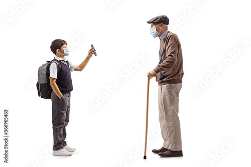 Schoolboy wearing a protective face mask and showing a mobile phone to an elderly man with a cane